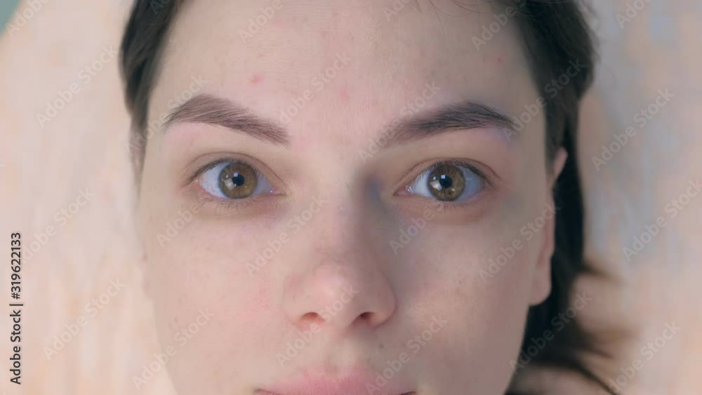 Portrait of woman after tinting eyebrows looking at camera in cosmetology clinic, face closeup. Young girl brunette with painted eyebrows. Portrait of woman after tinting eyebrows looking at camera in cosmetology clinic, face closeup. Young girl brunette with painted eyebrows.