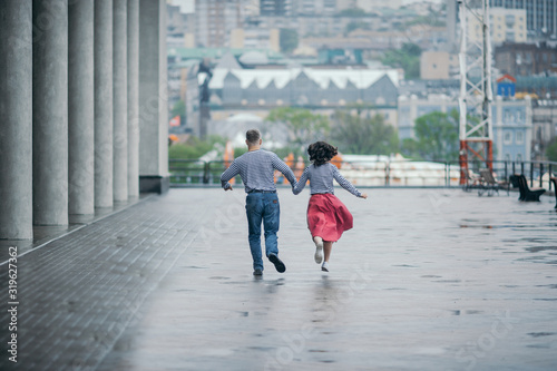 a pair of lovers in striped sweatshirts run away from everyone holding hands on a wet rainy day on a city street