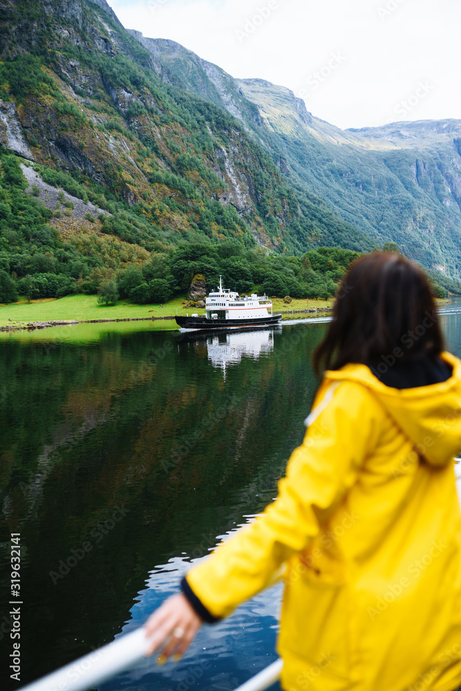 The girl tourist on a pleasure boat on the fjord enjoys the picturesque mountains and lakes of Norway. Young woman posing against the backdrop of the mountains. Travelling, lifestyle, adventure.