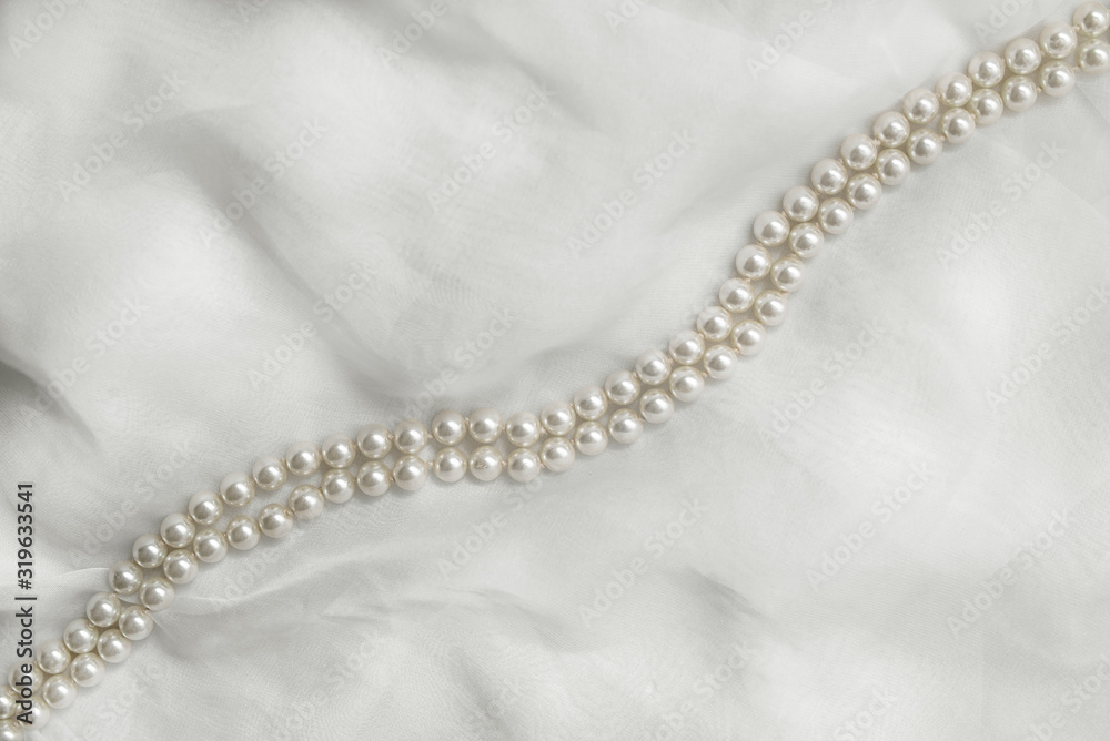 A necklace of pearls lies on a white cloth A necklace of pearls lies on a white cloth