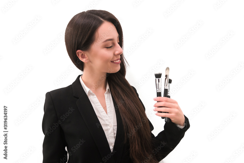 girl with make-up with long dark hair in a business suit holding a brush in his hand, on a white background girl with make-up with long dark hair in a business suit holding a brush in his hand, on a white background
