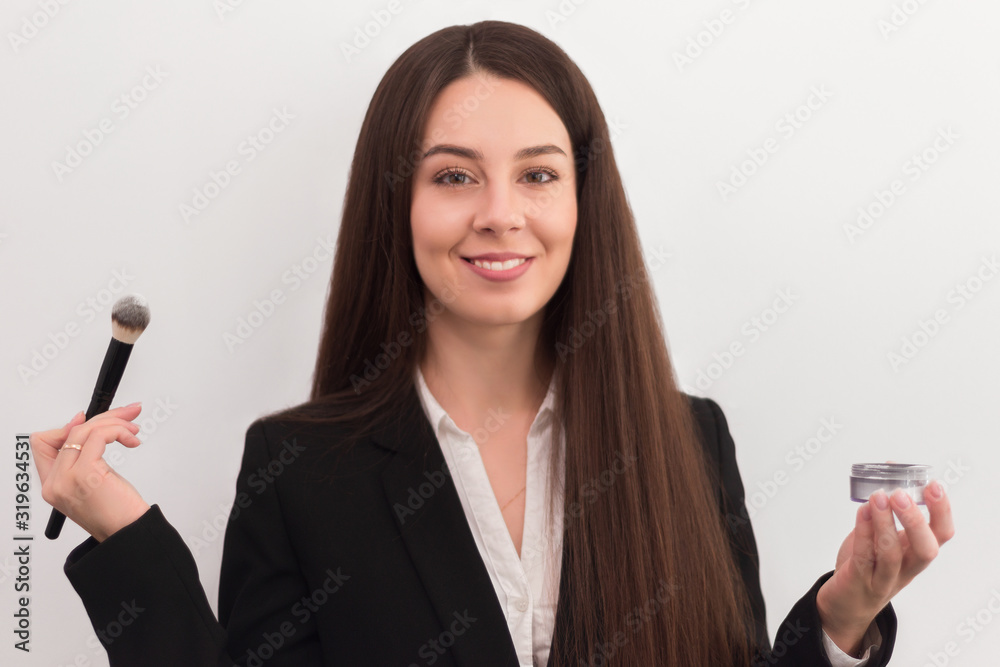 girl, makeup artist, with long dark hair in a business suit holding a brush and powder in his hands on a white background