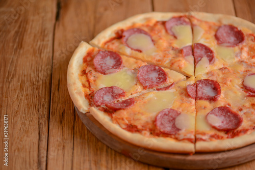 Flat lay pepperoni pizza isolated on rustic wooden background. Pizza salami cut in slices. Fast food, junk food concept.