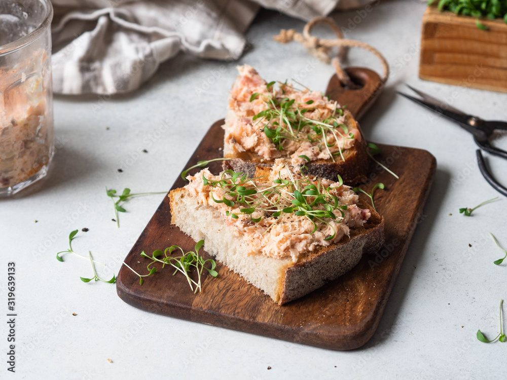 Healthy toasts with salmon pate and fresh green sprouts on yeast-free bread on wood cutting board on grey background. Copy space