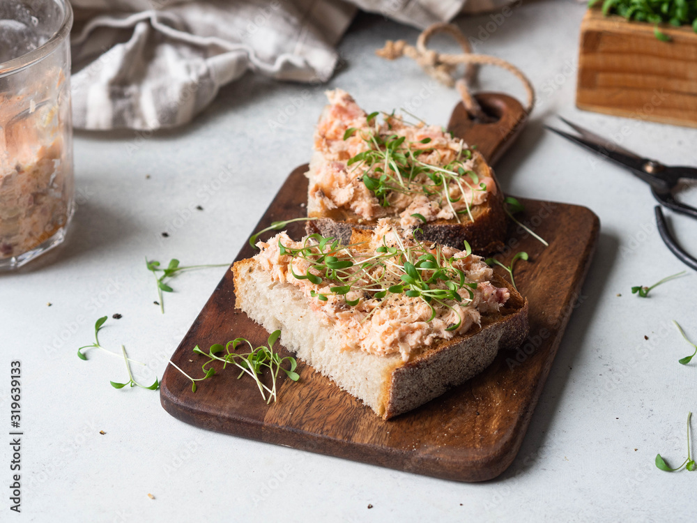 Healthy toasts with salmon pate and fresh green sprouts on yeast-free bread on wood cutting board on grey background. Copy space Healthy toasts with salmon pate and fresh green sprouts on yeast-free bread on wood cutting board on grey background. Copy space