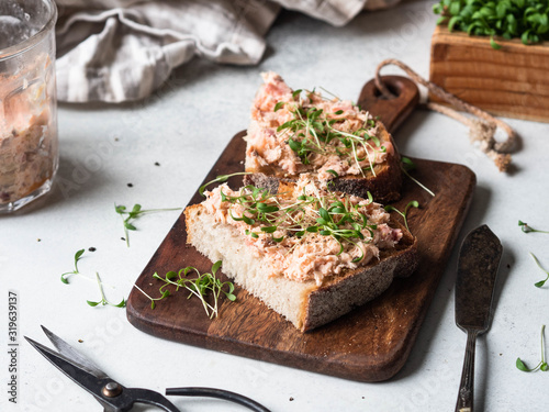 Healthy toasts with salmon pate and fresh green sprouts on yeast-free bread on wood cutting board on grey background. Copy space