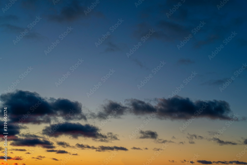 Evening sky at sunset background. Dark clouds hanging above horizon. Majestic cloudscape in blue, orange, violet shades. Grey cloudlets bringing rain. Countryside skyline in twilight time