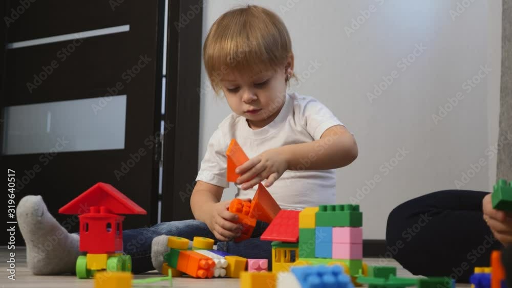 Blond little children play with bright cubes on the floor at home. Blond little children play with bright cubes on the floor at home.