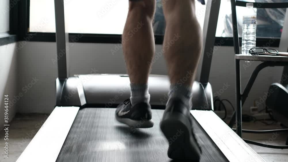 Close-up muscular feet in sneaker running on treadmill in gym Close-up muscular feet in sneaker running on treadmill in gym