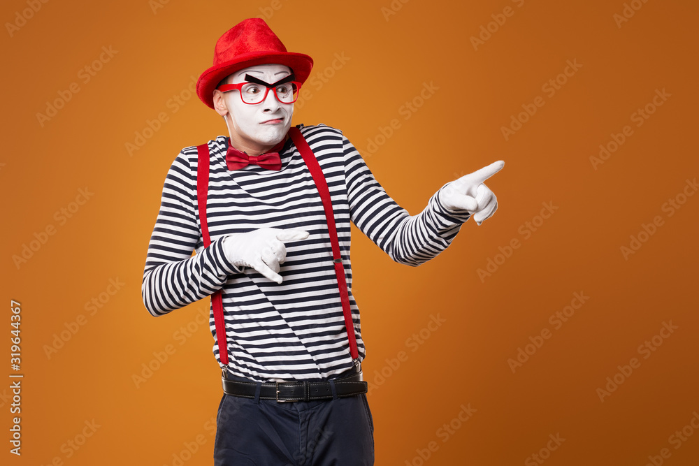 Seriouse mime man looking at camera in red hat and vest on orange background