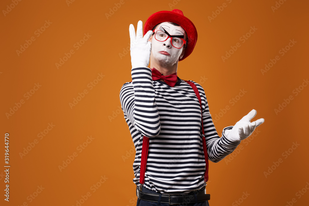 Mime male in vest and red hat with raised palms on orange background