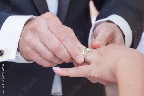 Wedding bride and groom couple at marriage ring vows ceremony. Husband with dark suit and wife with bright dress exchange golden luxury rings. Holding hands and put a ring on each others finger