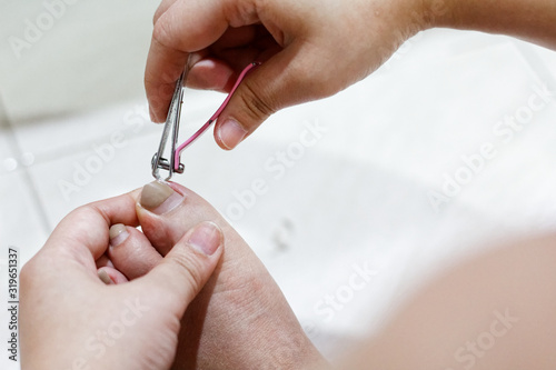 Asian woman cutting pedicure With a pink nail cutter. Painted toenails.