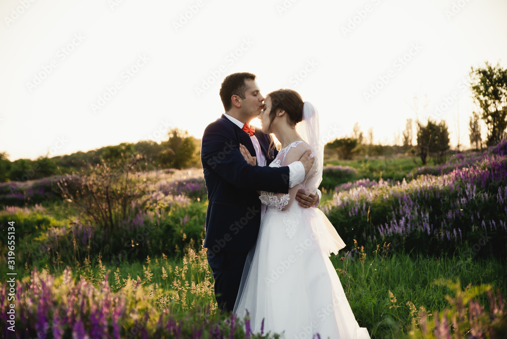 Bride and groom hugging at sunset,happy bride and groom smiling,happy bride and groom after the wedding ceremony,wedding day,beautiful young couple in a field with flowers,wedding day in the lives of 