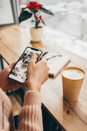 close-up of woman's hand holding a cellphone with empty copy space for your advertising text message or advertising content, hipster girl watching photos on a mobile phone during a coffee break.