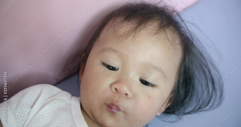 Baby in white shirt holding milk bottle lying in bed Baby in white shirt holding milk bottle lying in bed
