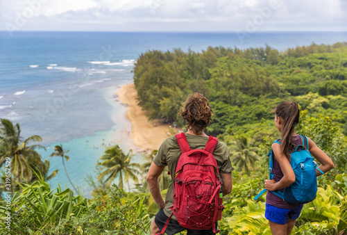 Hikers couple hiking on Kalalau trail overlooking beach coastal walk two tourists with backpacks walking outdoor in Kauai island, Hawaii summer travel leisure activity active lifestyle. photo