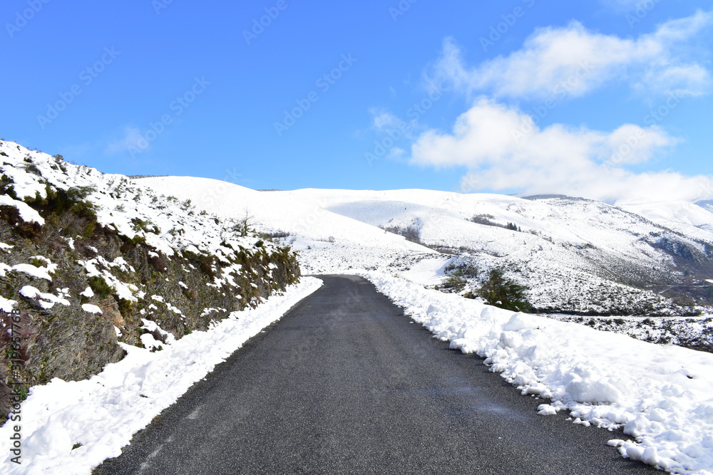 Winter landscape with road and snowy mountains with blue sky. Ancares, Lugo, Galicia, Spain.