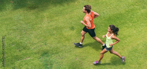 Run jog couple athletes training together doing running workout partner buddy jogging on green grass park lawn top view from drone. Asian woman and man runners.