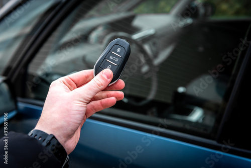 Hand holding a car key with remote control and pushing a button, he is unlocking the door.