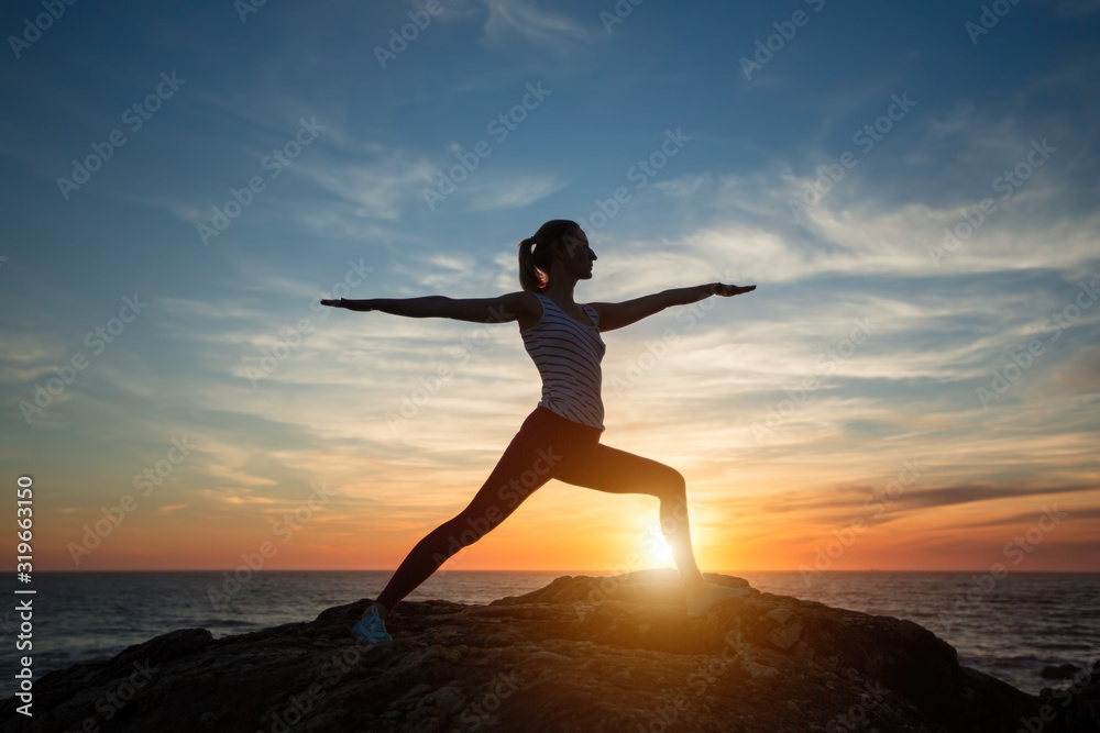 Fetness woman silhouette performs yoga exercises during amazing sunset on the sea coast.
