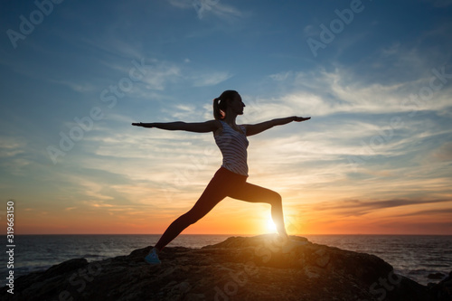 Fototapeta Naklejka Na Ścianę i Meble -  Fetness woman silhouette performs yoga exercises during amazing sunset on the sea coast.