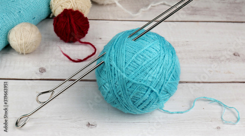 A large Tangle of light blue woolen threads for hand knitting with stuck into it knitting needles close-up and several small balls of yarn in the background on a white wooden table.