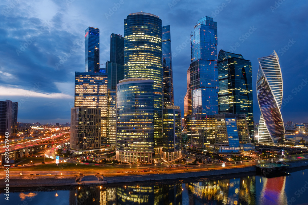 Obraz premium Business district of the city. Night photography of the financial center of Moscow. Skyscrapers shimmering with colorful lights. Reflection in the water of the river.