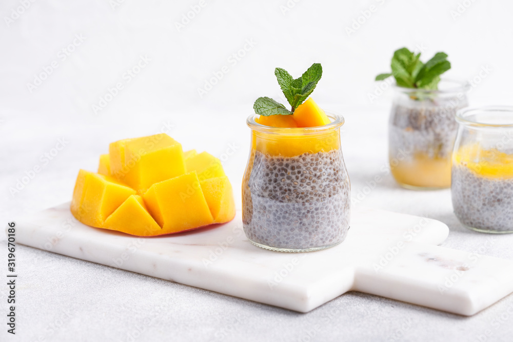 Chia seeds pudding with mango puree in glasses with green mint leaves and cut fresh ripe tropical fruit on light white background. Raw vegetarian sweet organic dessert. Copy space for text