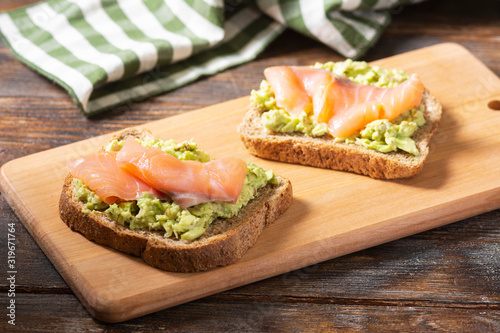 Bruschetta with avocado and salmon on a wooden Board on a brown wooden table. Toasted bread with avocado and red fish. The concept is useful and delicious Breakfast