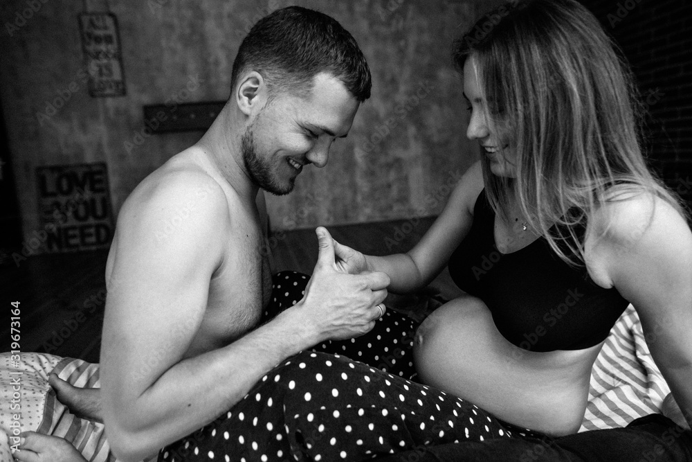 Beautiful pregnant woman and her handsome husband are smiling while spending time together in bed. Man is listening to baby in belly Beautiful pregnant woman and her handsome husband are smiling while spending time together in bed. Man is listening to baby in belly