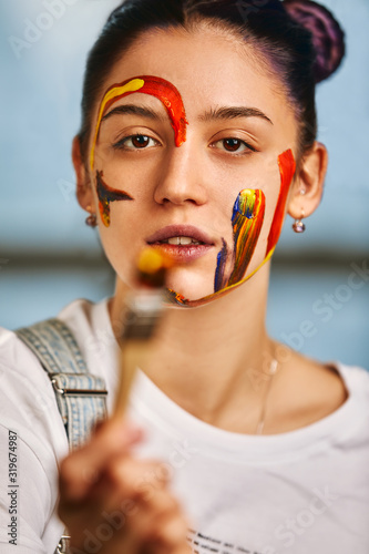 Portrait of a beautiful girl in the paint. Half-length portrait of the artist's girl with face and hands with different colors. Fashion art concept, beauty, creative people, freelance people