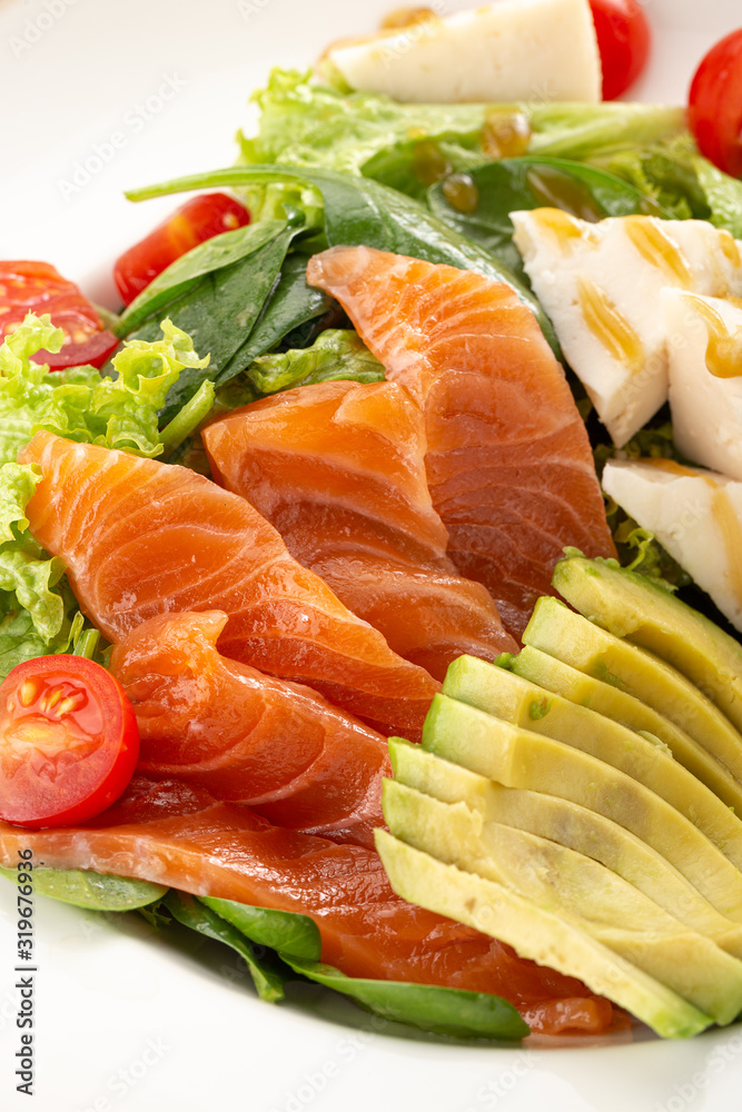 Delicious fresh salad. Salad with salmon, avocado, lettuce, tomatoes, parmesan, cheese, spinach. Fresh salmon salad with avocado and vegetables. Close up view on Salad