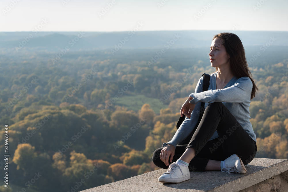 Beautiful girl sits on a hill and looks into the distance. Enjoyment of nature