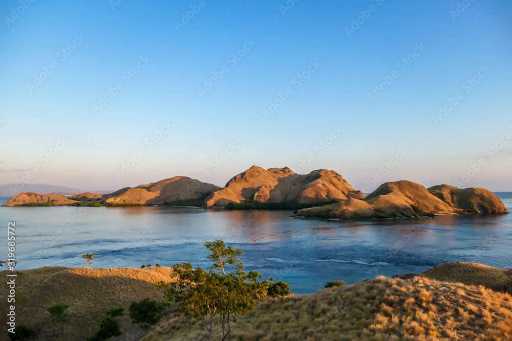 Fototapeta premium A view on a the morning sun rising over an island formation in Komodo National Park, Flores, Indonesia. Golden hour over the islands and sea. Idyllic landscape. New day beginning. Chocolate hills.