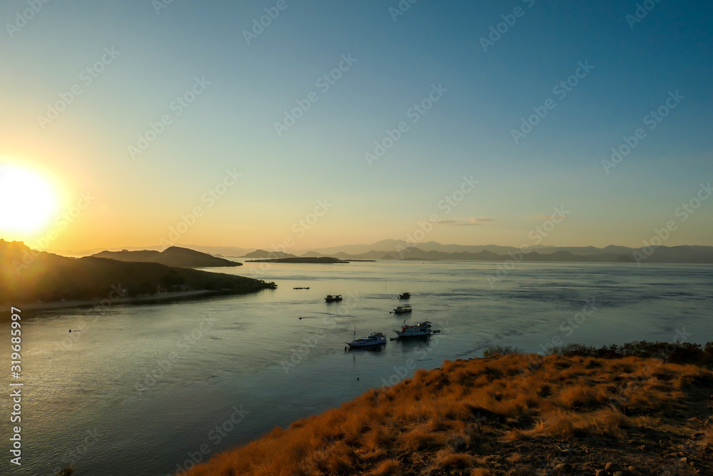 A view on a the morning sun rising over an island formation in Komodo National Park, Flores, Indonesia. Golden hour over the islands and sea. Idyllic landscape. New day beginning. Chocolate hills.