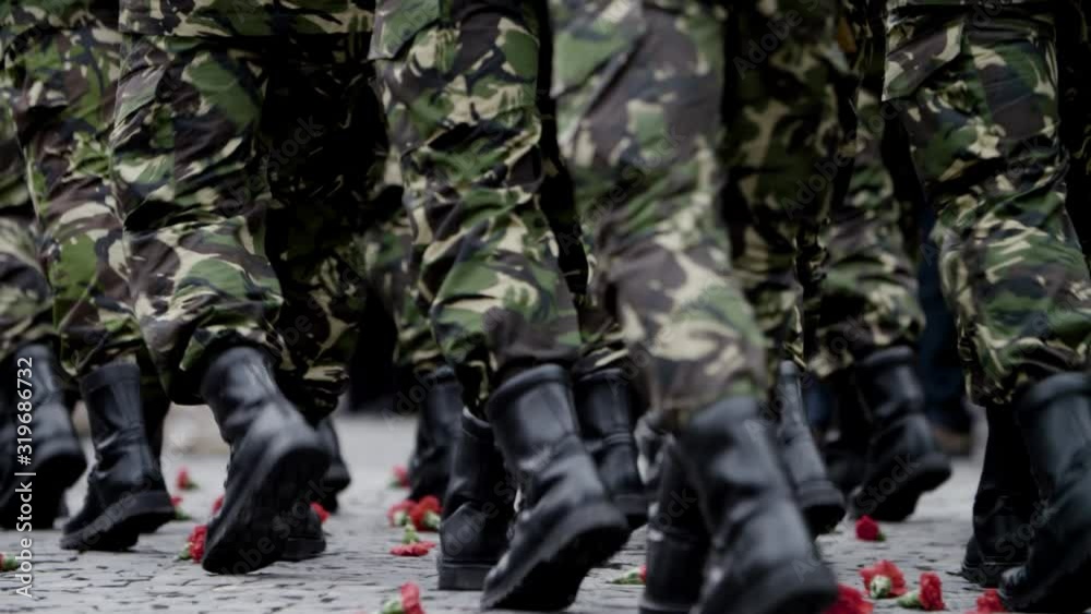 Close up of military men maching on cobblestone and stepping over red carnations