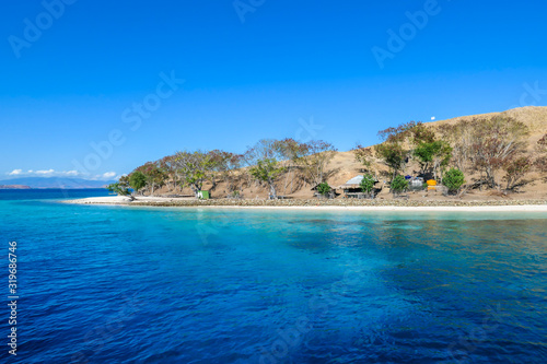 A panoramic view of idyllic white sand beach in Komodo National Park, Flores, Indonesia. Beach is gently washed by waves. Island has scarcely any plants on it. Idyllic location. Serenity and calmness