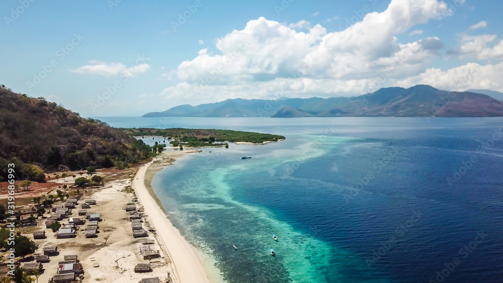 A drone shot of a small island near Maumere, Indonesia. There is a small fisherman's village next to the beach. Few boats anchored to the shores of the white sand beach. Calmness and serenity.