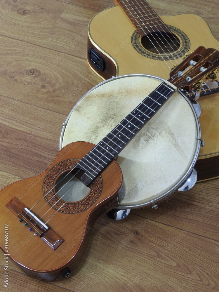 Naklejka premium Close-up of an acoustic guitar and two Brazilian musical instruments: cavaquinho and pandeiro (tambourine), on a wooden surface. The instruments are widely used to accompany samba and choro music.
