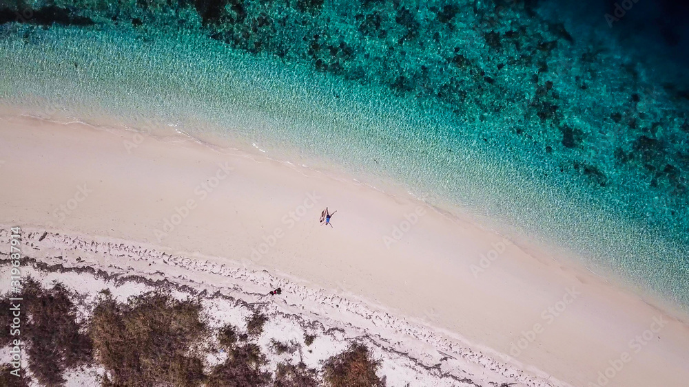 A drone shot of a couple sitting on a pink sand beach on a small island near Maumere, Indonesia. Happy and careless moments. Waves gently washing the shore. Romance and love while travelling