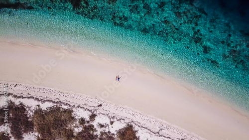 A drone shot of a couple sitting on a pink sand beach on a small island near Maumere, Indonesia. Happy and careless moments. Waves gently washing the shore. Romance and love while travelling photo