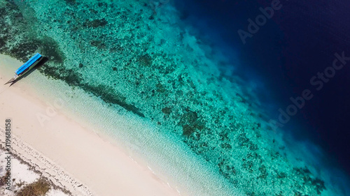 A drone shot of a boat anchored to pink sand beach on a small island near Maumere, Indonesia. Happy and careless moments. Waves washing the shore. Clear, turquoise coloured water displaying coral reef
