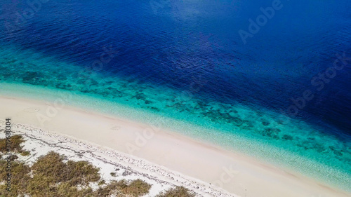 A drone shot of a pink sand beach on a small island near Maumere, Indonesia. Happy and careless moments. Waves gently washing the shore.Clear, turquoise coloured water displaying coral reef.