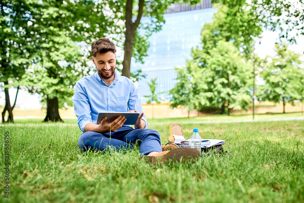 Fototapeta premium Happy young man using tablet while sitting outdoor in the park