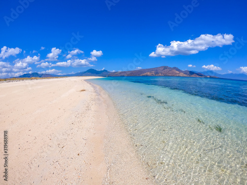 Fototapeta Naklejka Na Ścianę i Meble -  A view on white sand beach on a small island near Maumere, Indonesia. Happy and careless moments. Waves gently washing the shore. Clear, turquoise coloured water displaying coral reef. Hidden gem.