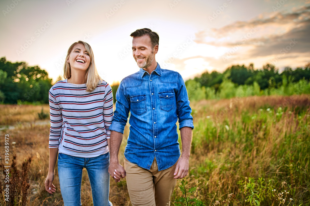 Smiling couple walking through meadow on sunny day and holding hands Smiling couple walking through meadow on sunny day and holding hands