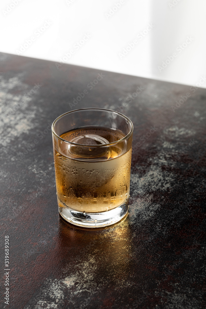 wet glass with strong whiskey and ice cube on black surface wet glass with strong whiskey and ice cube on black surface
