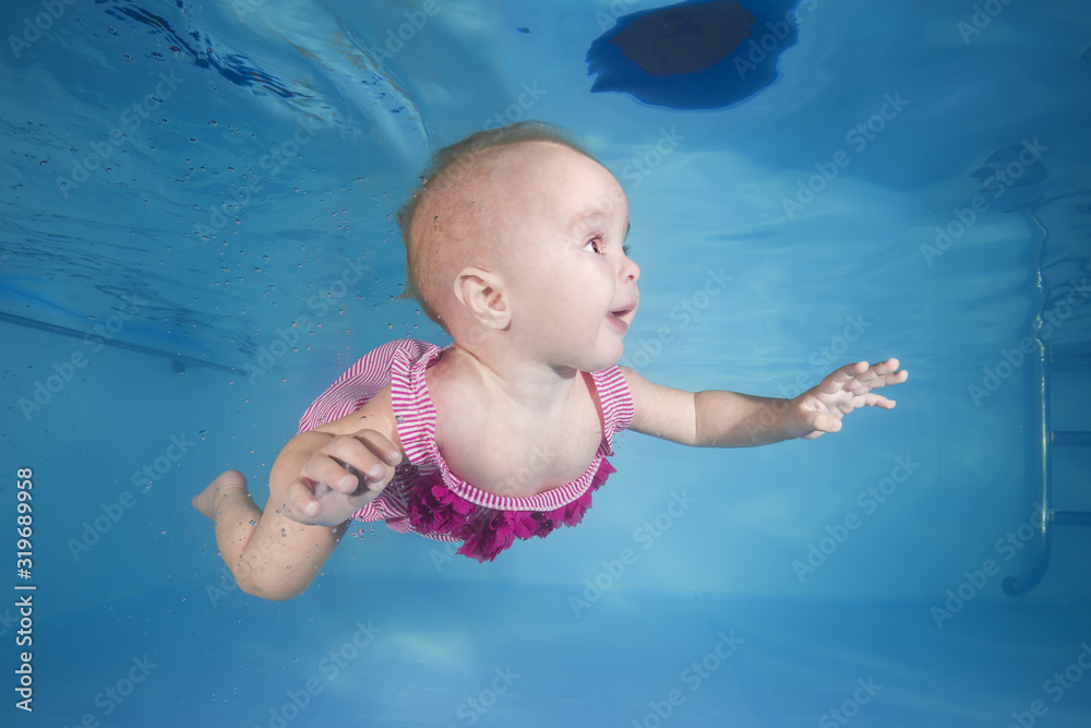 little girl in a pink swimsuit learns to dive underwater in the swimming pool