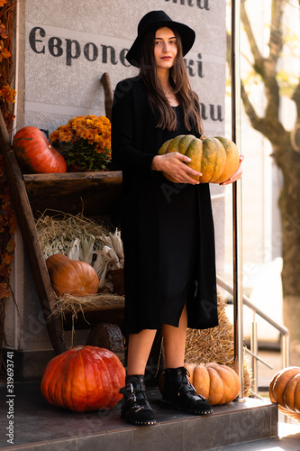 Photo of brunette lady posing on halloween concept background with pumpkins.Fashion style portrait. Girl wearing dark casual dress and dark hat .Fashion concept. Witch costume